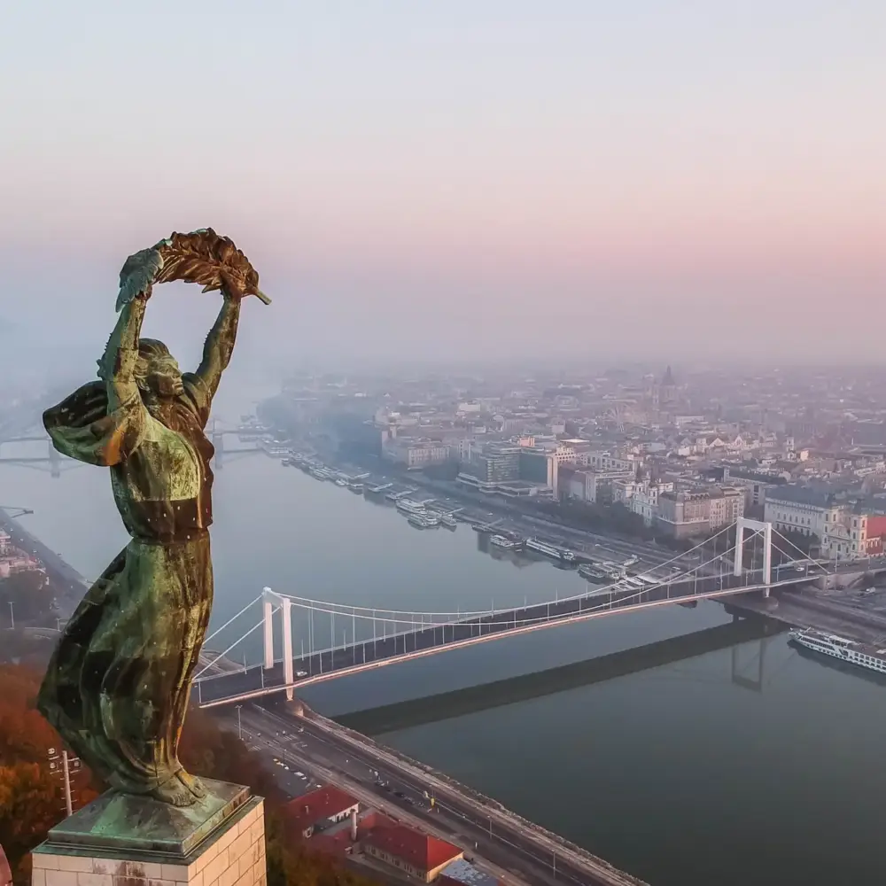 Aerial view to the Statue of Liberty with Elisabeth Bridge and River Danube taken from Gellert Hill on sunrise in fog in Budapest, Hungary. Drone shot