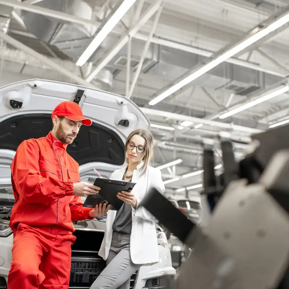 Young woman client with auto mechanic in red uniform standing with some documents at the car service. Wide view with copy space